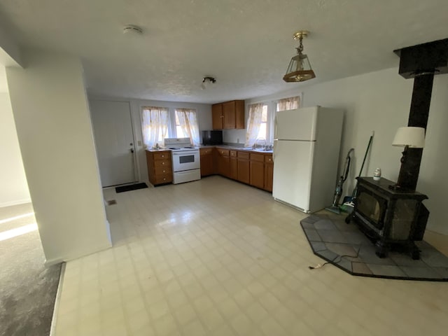 kitchen featuring a textured ceiling, white appliances, sink, a wood stove, and hanging light fixtures