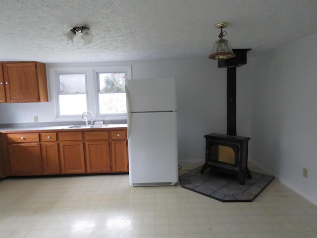 kitchen with a wood stove, sink, white fridge, a textured ceiling, and decorative light fixtures