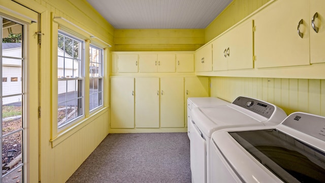 clothes washing area with washer and clothes dryer, cabinets, light carpet, and wooden walls