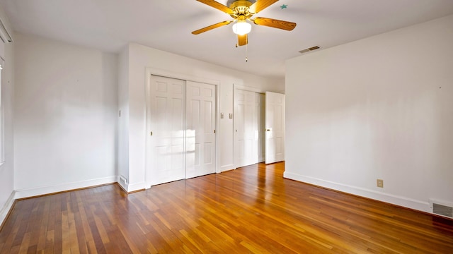 unfurnished bedroom with ceiling fan, hardwood / wood-style floors, and two closets