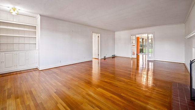 unfurnished living room featuring crown molding, built in features, and hardwood / wood-style flooring