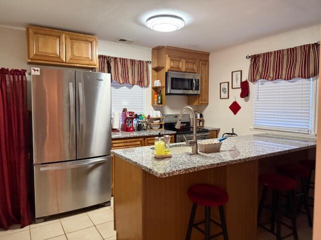 kitchen with a center island with sink, light stone counters, light tile patterned floors, and appliances with stainless steel finishes