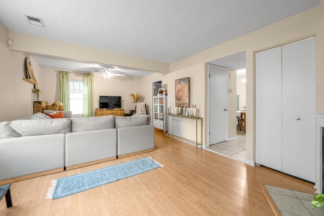 living room with ceiling fan, a textured ceiling, and light hardwood / wood-style flooring