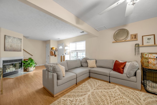 living room with beamed ceiling, ceiling fan, light hardwood / wood-style floors, and a textured ceiling