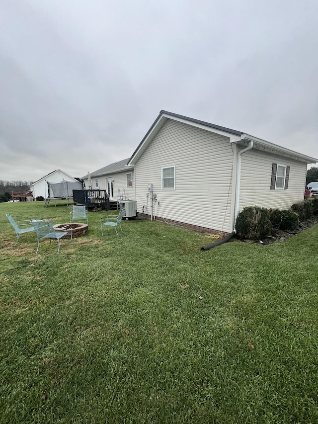 view of side of home with a fire pit, a lawn, and central air condition unit