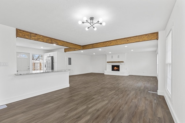 unfurnished living room featuring beam ceiling, an inviting chandelier, a brick fireplace, dark hardwood / wood-style flooring, and a textured ceiling