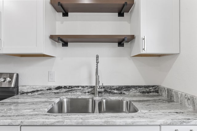 interior details with white cabinetry, sink, and light stone countertops