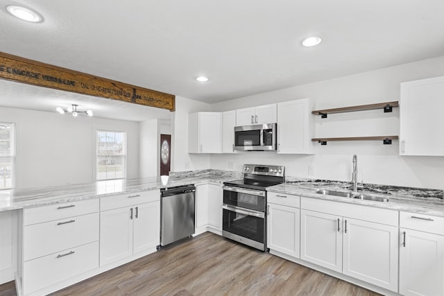 kitchen featuring kitchen peninsula, appliances with stainless steel finishes, light wood-type flooring, sink, and white cabinetry