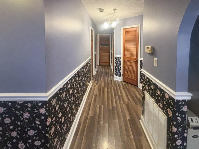 hall with a textured ceiling, a notable chandelier, and dark wood-type flooring