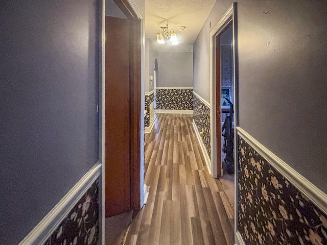 hall with hardwood / wood-style floors, a textured ceiling, and an inviting chandelier