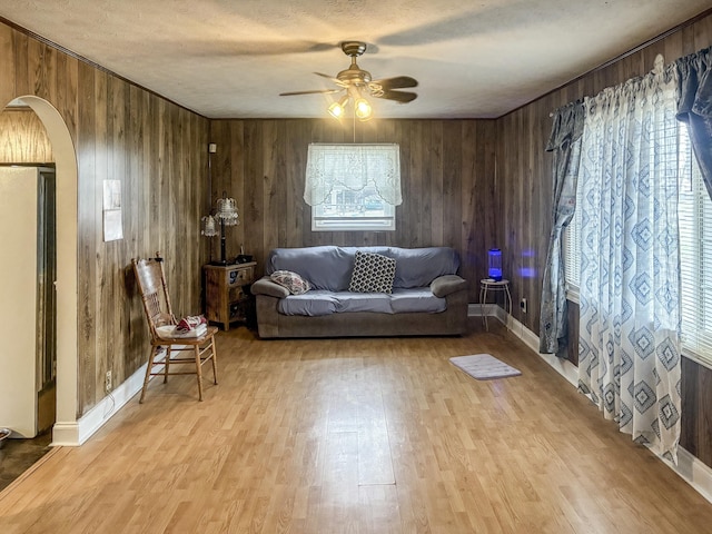 living room featuring wood walls, ceiling fan, light hardwood / wood-style floors, and a healthy amount of sunlight