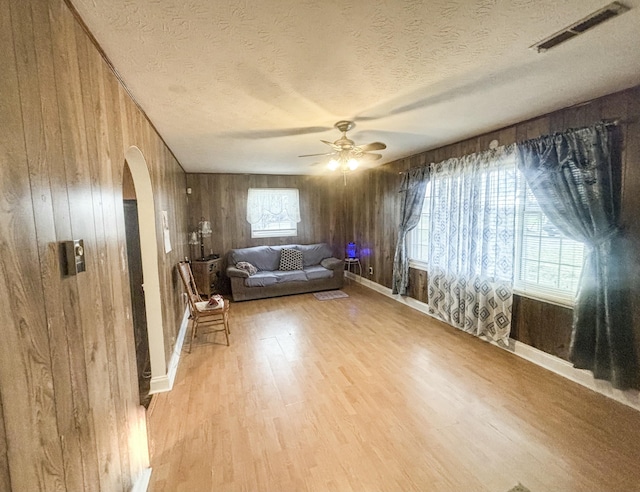 unfurnished living room featuring wood walls, ceiling fan, a healthy amount of sunlight, and light hardwood / wood-style flooring