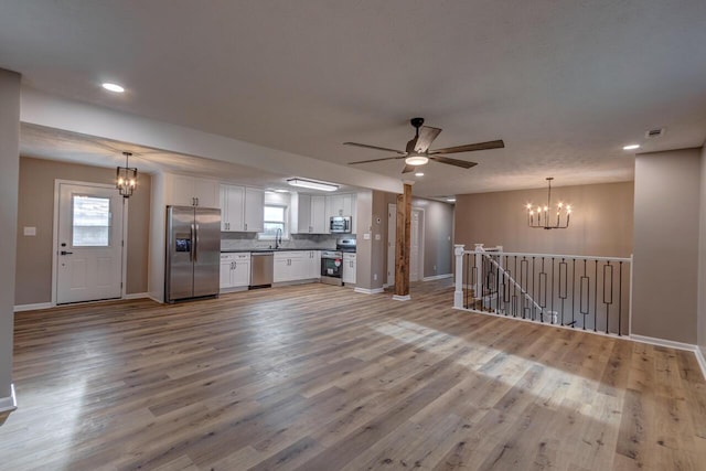 unfurnished living room featuring sink, ceiling fan with notable chandelier, and light wood-type flooring