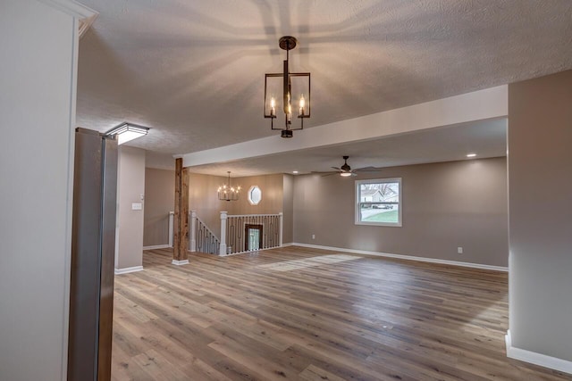 unfurnished living room with ceiling fan with notable chandelier, a textured ceiling, and hardwood / wood-style flooring