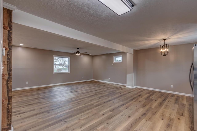 unfurnished room featuring a textured ceiling, ceiling fan with notable chandelier, and light hardwood / wood-style flooring