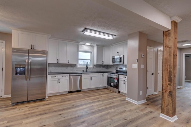 kitchen with backsplash, sink, light hardwood / wood-style flooring, appliances with stainless steel finishes, and white cabinetry