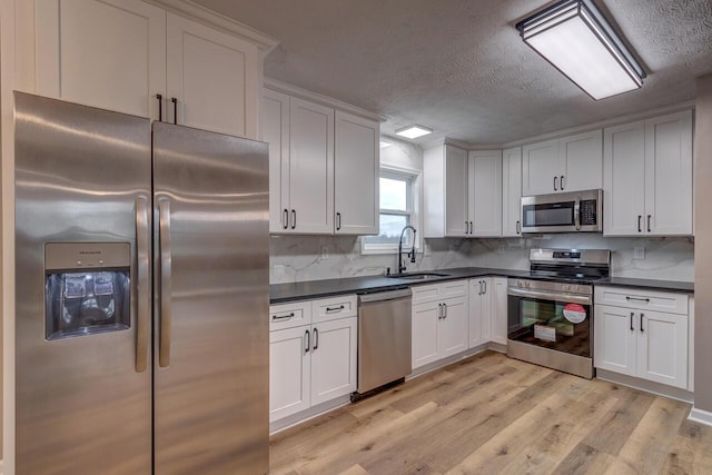 kitchen featuring sink, light hardwood / wood-style flooring, decorative backsplash, white cabinets, and appliances with stainless steel finishes