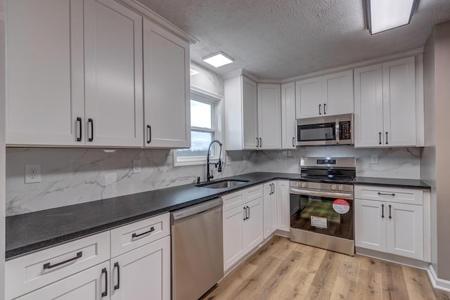 kitchen with sink, decorative backsplash, light wood-type flooring, appliances with stainless steel finishes, and white cabinetry