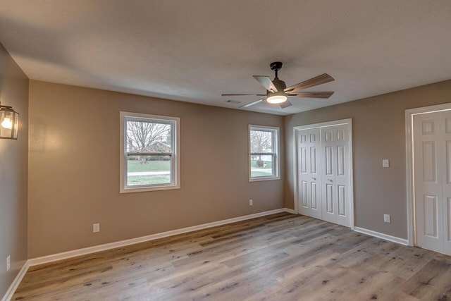 unfurnished bedroom with ceiling fan, light wood-type flooring, a textured ceiling, and multiple windows