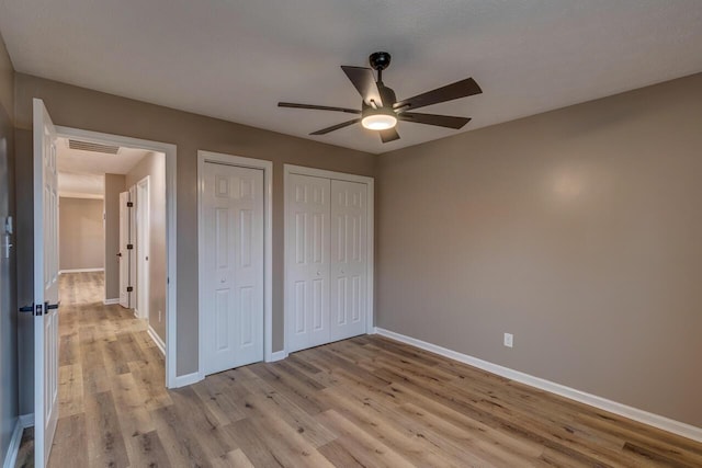 unfurnished bedroom with multiple closets, ceiling fan, and light hardwood / wood-style flooring