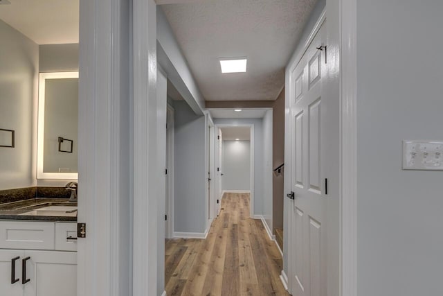 corridor with a textured ceiling, light hardwood / wood-style floors, and sink