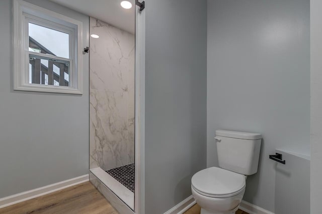 bathroom with hardwood / wood-style flooring, toilet, and a tile shower