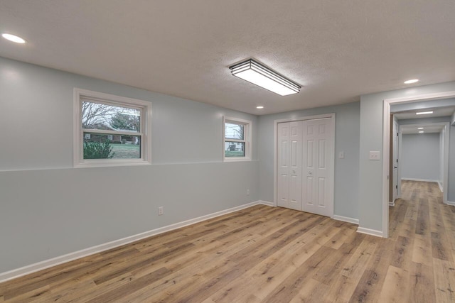 basement featuring a textured ceiling, light hardwood / wood-style floors, and a healthy amount of sunlight