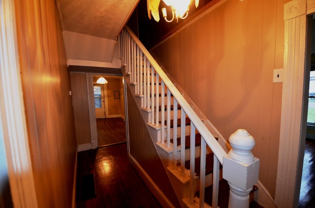 stairs featuring wood-type flooring, wooden walls, and a notable chandelier