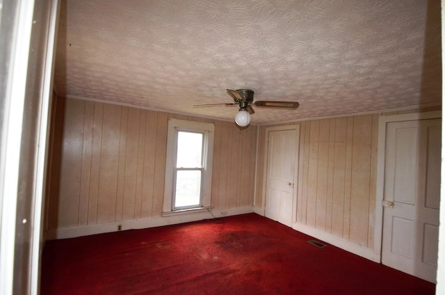 carpeted spare room with a textured ceiling, ceiling fan, and wood walls