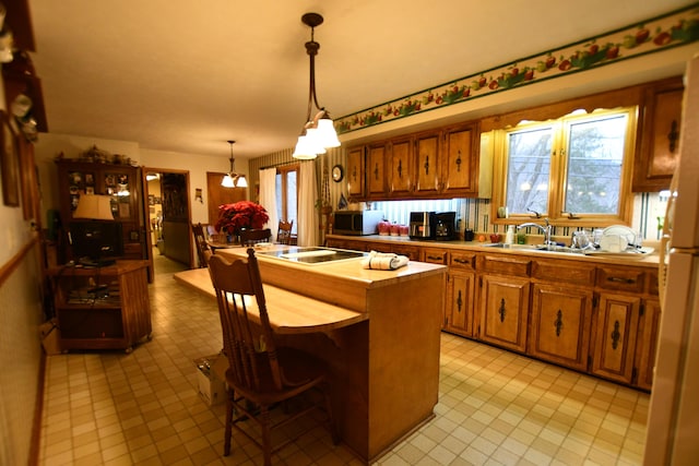 kitchen with a healthy amount of sunlight, decorative light fixtures, sink, cooktop, and a center island