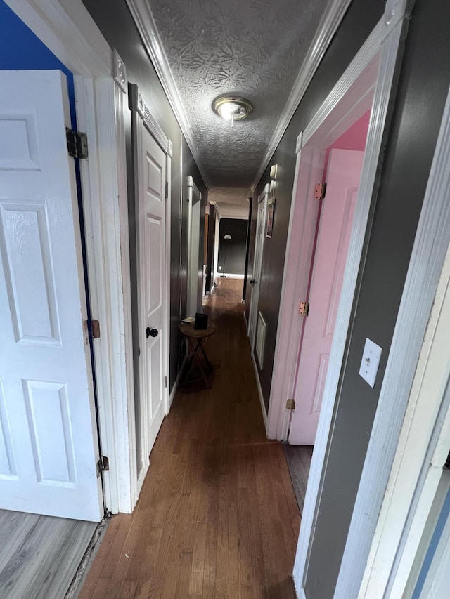 corridor featuring a textured ceiling, dark wood-type flooring, and crown molding