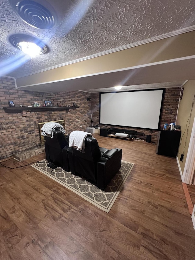 home theater with hardwood / wood-style floors, ornamental molding, a textured ceiling, and brick wall