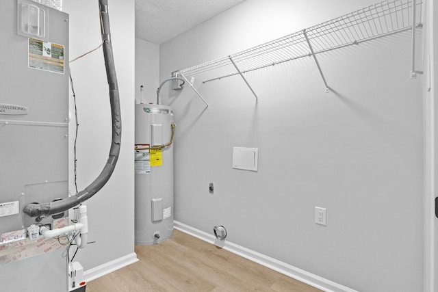 clothes washing area with electric dryer hookup, light hardwood / wood-style floors, a textured ceiling, and water heater