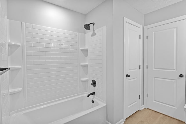 bathroom featuring a textured ceiling, hardwood / wood-style flooring, and tiled shower / bath