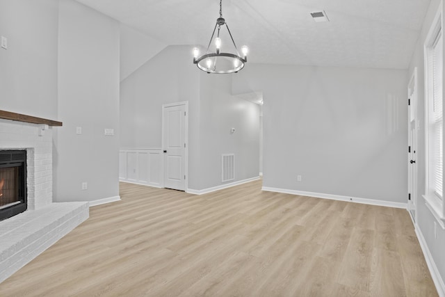 unfurnished living room featuring light wood-type flooring, a fireplace, high vaulted ceiling, and an inviting chandelier