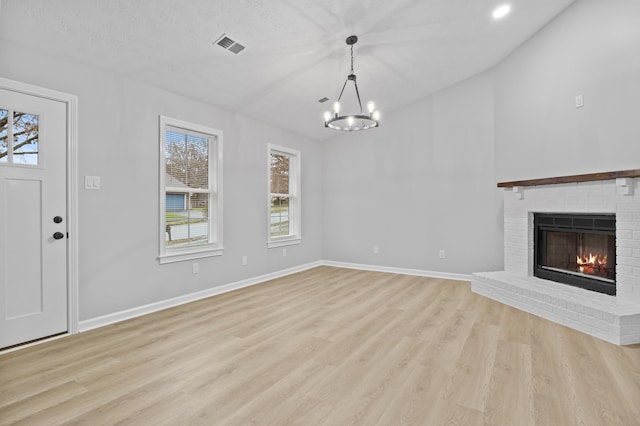 unfurnished living room with light wood-type flooring, a brick fireplace, and plenty of natural light