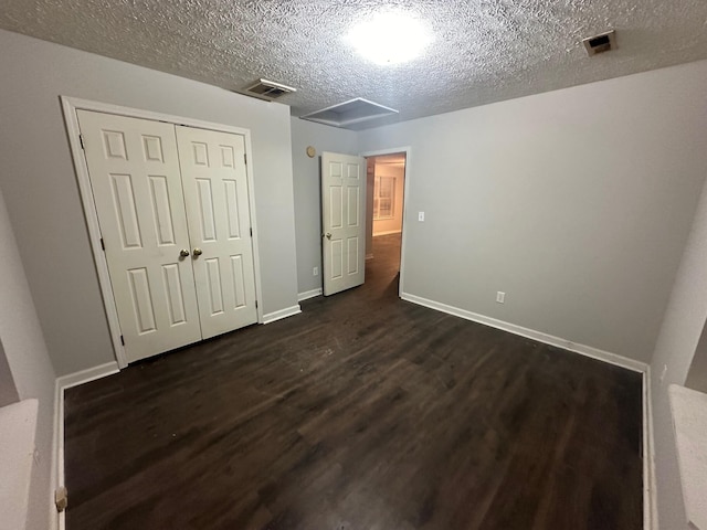 unfurnished bedroom with a textured ceiling, dark hardwood / wood-style flooring, and a closet