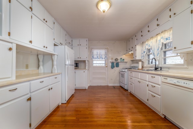 kitchen with white cabinetry, hardwood / wood-style floors, white appliances, and sink