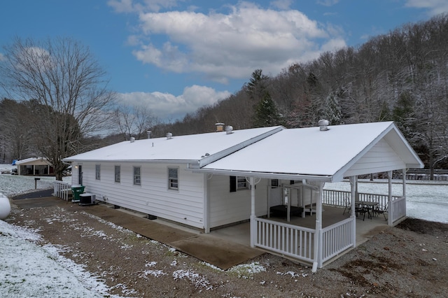 snow covered rear of property with covered porch and central AC