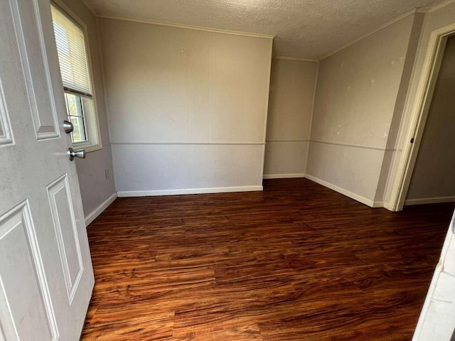 empty room featuring dark wood-type flooring, a textured ceiling, and ornamental molding