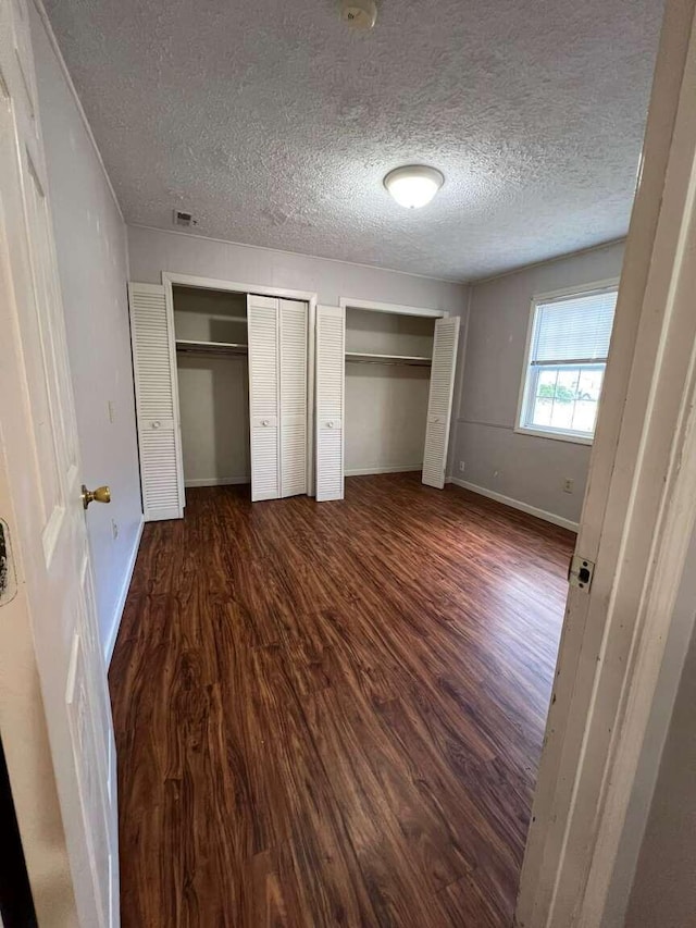 unfurnished bedroom with a textured ceiling, multiple closets, and dark hardwood / wood-style floors