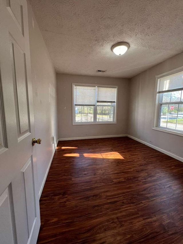 unfurnished room with dark hardwood / wood-style floors, a healthy amount of sunlight, and a textured ceiling