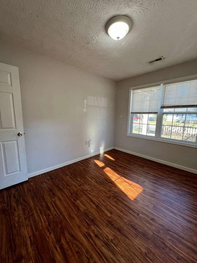 spare room featuring a textured ceiling and dark hardwood / wood-style floors