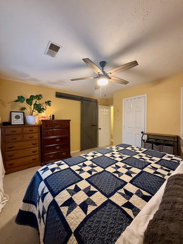 bedroom with ceiling fan, light colored carpet, a barn door, and a textured ceiling