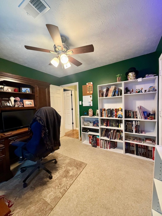 carpeted home office with ceiling fan and a textured ceiling