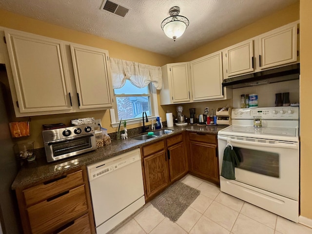 kitchen with sink, a textured ceiling, light tile patterned floors, white appliances, and dark stone counters