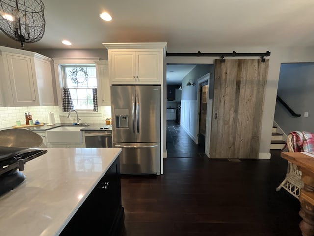 kitchen with a barn door, white cabinetry, hanging light fixtures, and stainless steel appliances