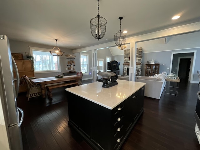 kitchen featuring dark wood-type flooring, a stone fireplace, white fridge, decorative light fixtures, and a kitchen island