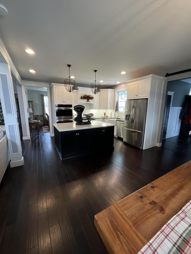 kitchen with a center island, white cabinets, hanging light fixtures, dark hardwood / wood-style floors, and appliances with stainless steel finishes