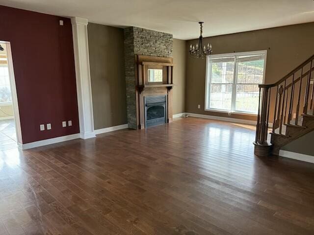 unfurnished living room with a stone fireplace, dark hardwood / wood-style flooring, and an inviting chandelier